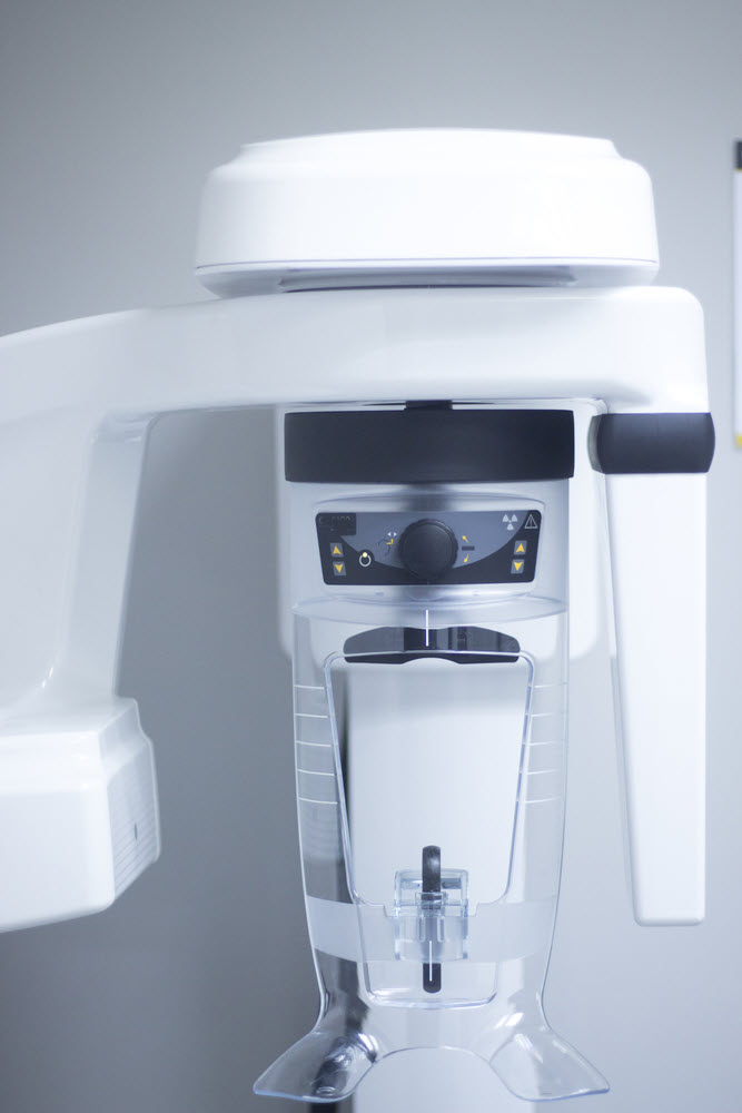 An image of a high-tech x-ray machine. The machine is mostly white, used for taking 360 degree x-rays around the patient's head when they are standing up,